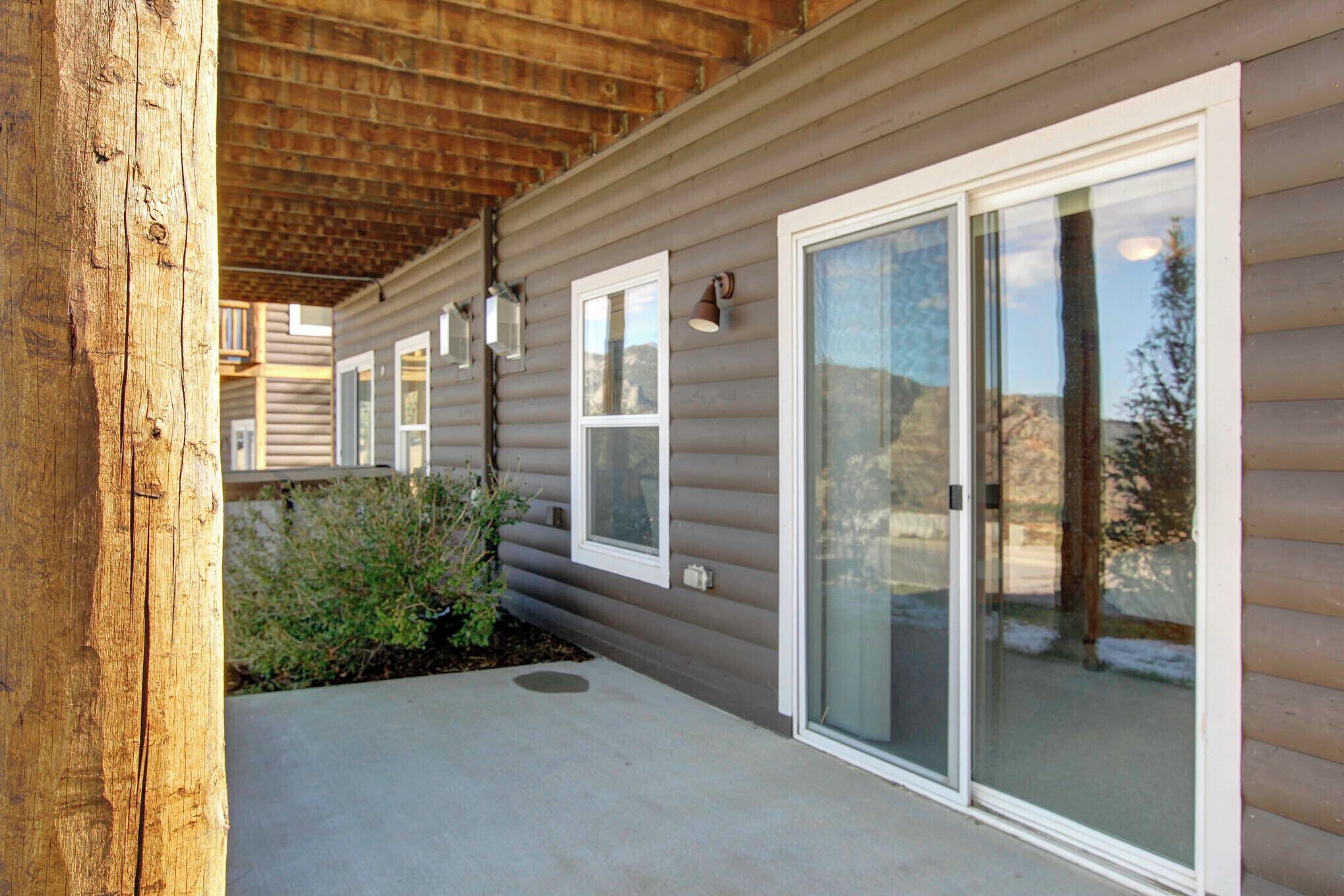 A covered patio area with a wooden ceiling, a sliding glass door, and a small garden with plants.