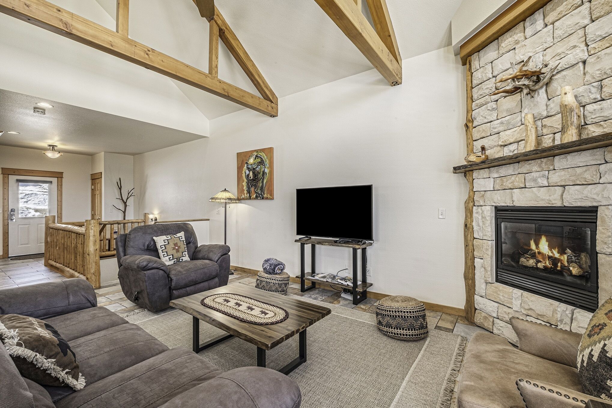 A cozy living room with a stone fireplace, a flat-screen TV, and comfortable seating.