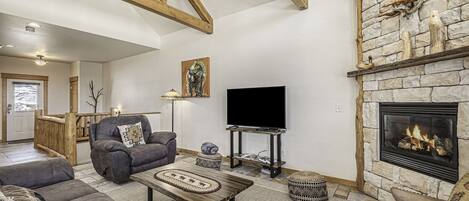 A cozy living room with a stone fireplace, a flat-screen TV, and comfortable seating.