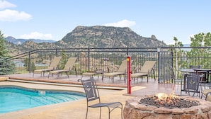 A pool area with lounge chairs and a fire pit, surrounded by a deck and a mountain view. - Estes Park Vacation Lodging (Estes Park)
