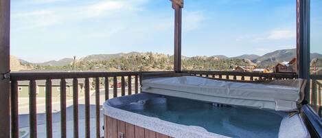 A hot tub on a wooden deck with a view of mountains and houses.