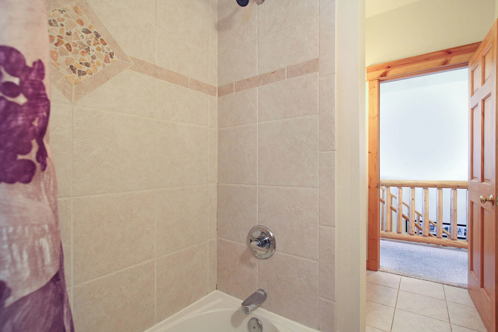 A bathroom with beige tiles, a shower, and a wooden door leading to a balcony.
