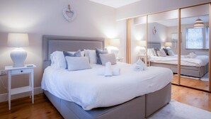 A modern bedroom with a large bed, bedside tables, a mirror, and a view of the adjacent room.