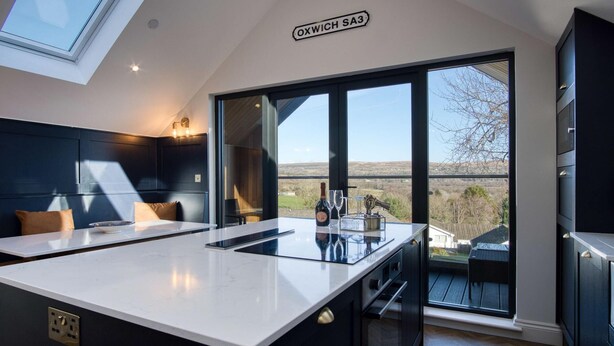 Une cuisine moderne dotée d’un grand îlot central, d’une verrière et offrant une vue sur la campagne.