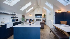 Une cuisine spacieuse dotée d’un grand îlot central, de fenêtres de toit et d’un coin salon confortable avec une cheminée.