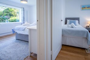 Een hotelkamer met twee bedden, een groot raam met uitzicht op groen en een schilderij aan de muur.