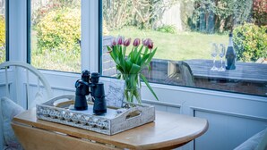 Een tafel met verrekijkers, een kaart en een vaas tulpen bij een raam met uitzicht op een tuin.