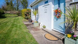 Een wit gebouw met een blauwe deur, een welkomstbord en een kleine tuin met bloempotten en bloemen.