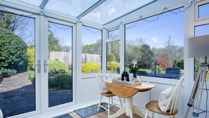 Een tuinkamer met een houten tafel en stoelen, een kleed en uitzicht op de tuin.