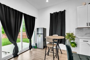 A modern kitchen with a refrigerator, a dining table with chairs, and black curtains.