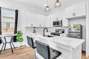 A modern kitchen with white cabinets, a central island, a microwave, a refrigerator, and pendant lights.