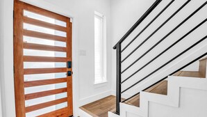 Eine Treppe mit weißen Wänden und Holzdielen, die zu einer Tür mit horizontalen Lamellen führt.