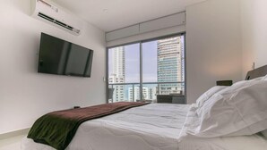 Una habitación de hotel moderna con una cama grande, un televisor de pantalla plana en la pared y un amplio ventanal con vistas a la ciudad.