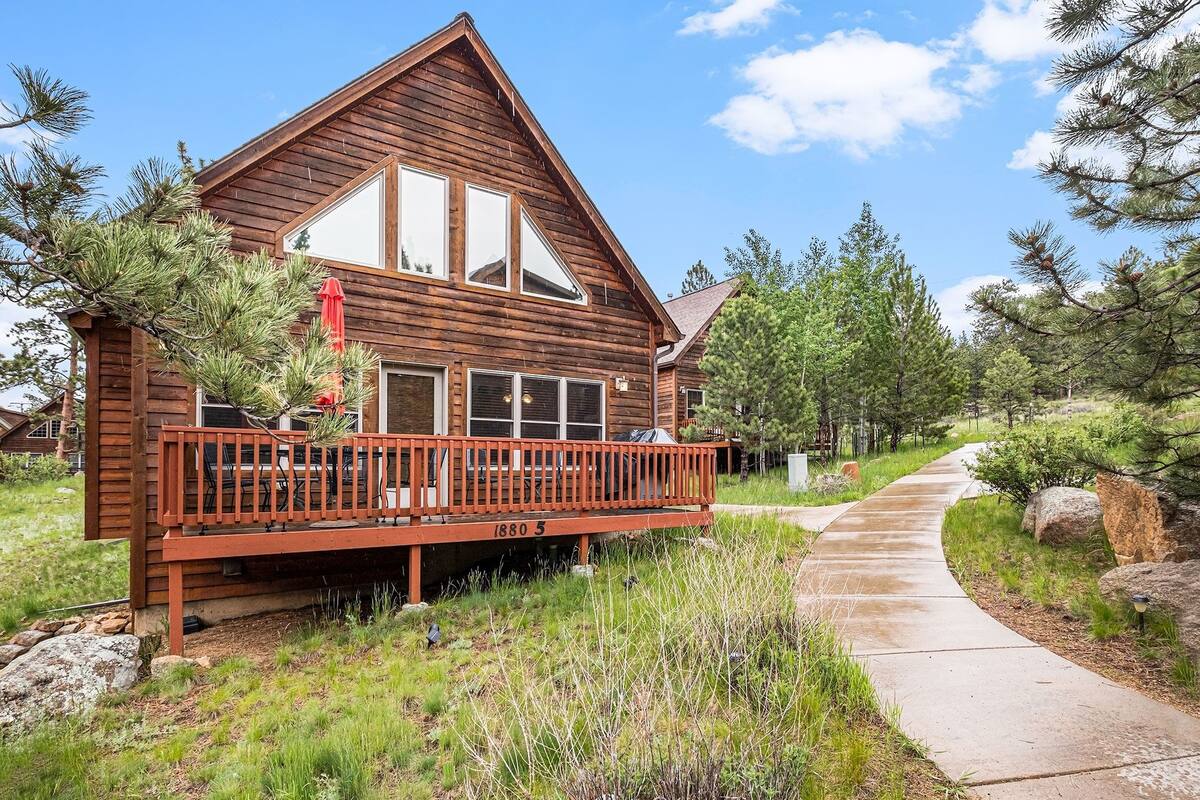 A wooden cabin with a balcony, surrounded by trees and a clear sky.