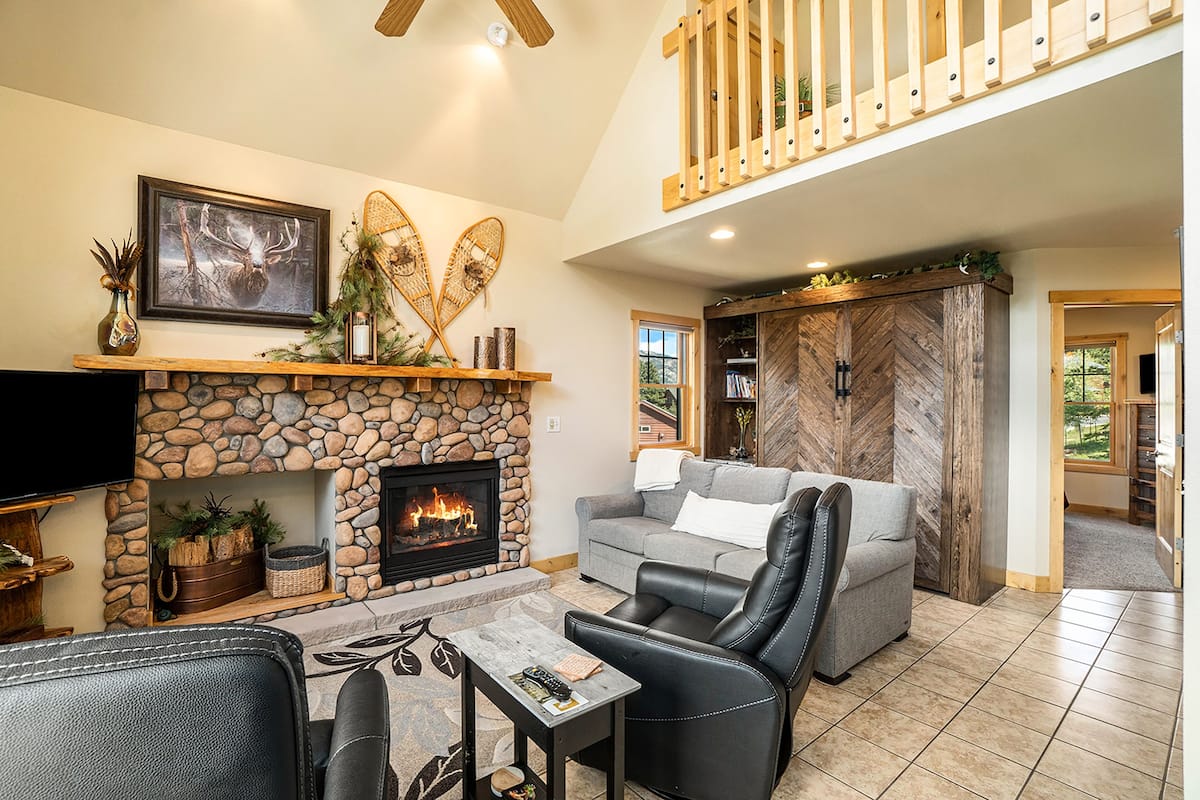 A living room with a stone fireplace, a gray sofa, a leather chair, and a television.