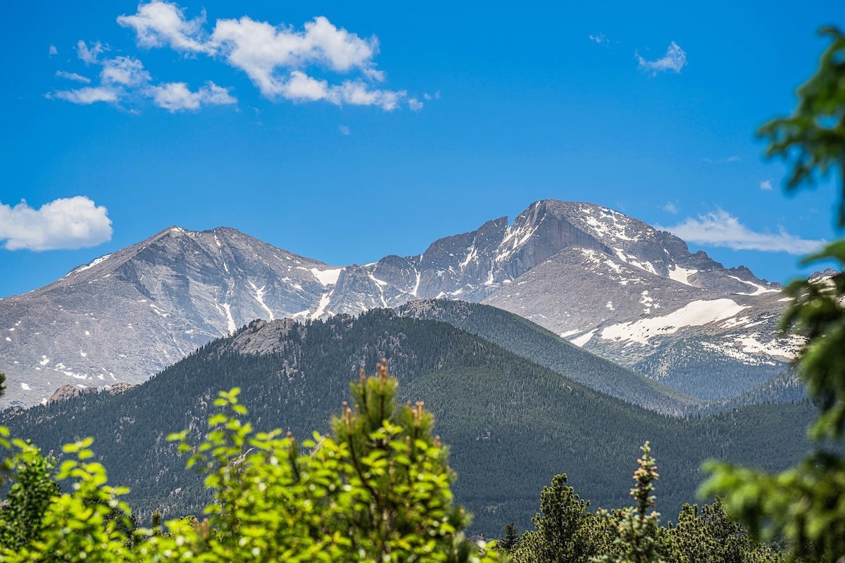 A mountain landscape with snow-capped peaks and dense forest in the foreground.