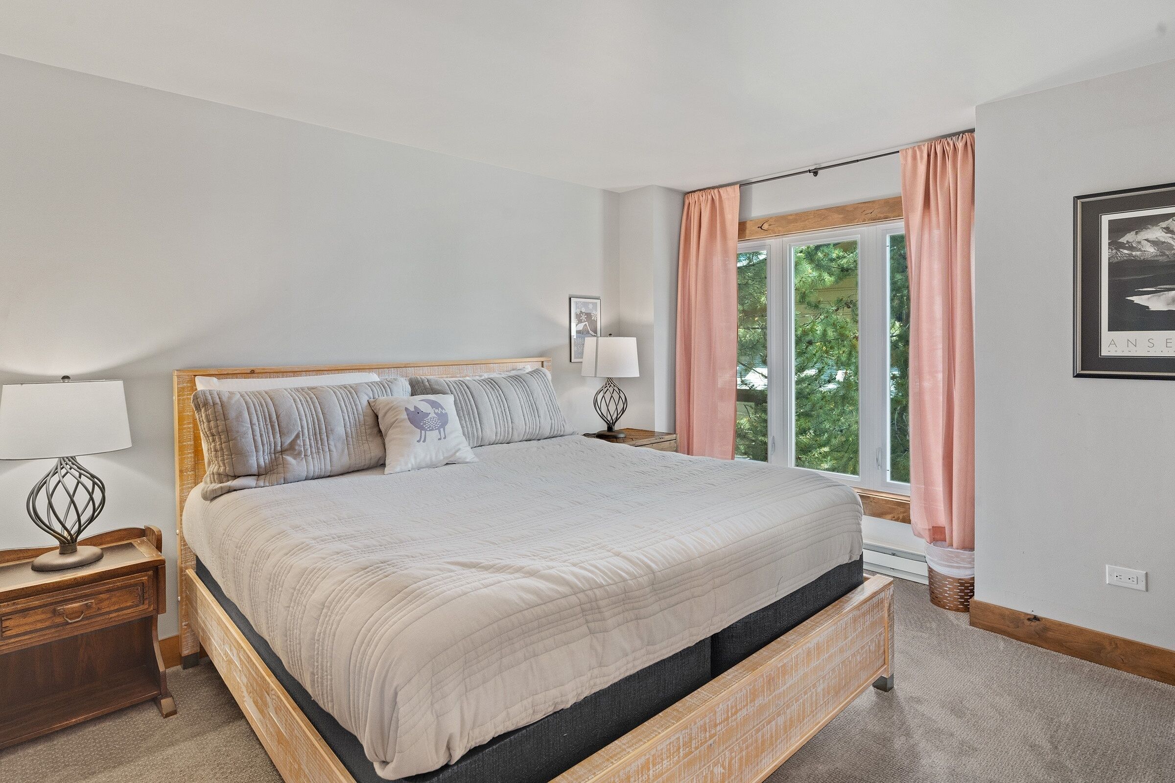 Une chambre à coucher avec un grand lit, une table de chevet avec une lampe, une fenêtre avec des rideaux et un tableau encadré au mur.