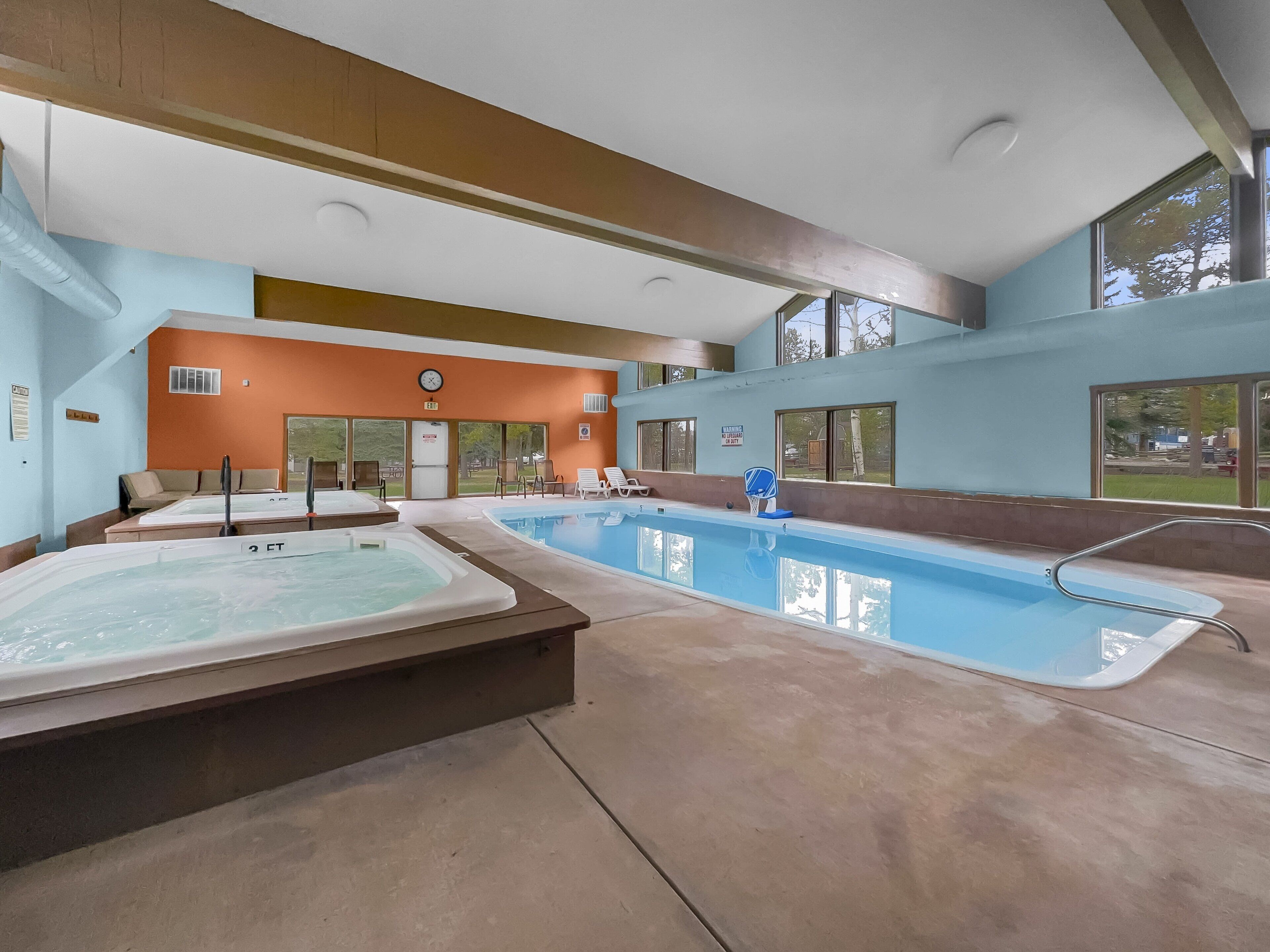 An indoor swimming pool with a hot tub, lounge chairs, and a view of the outdoors.