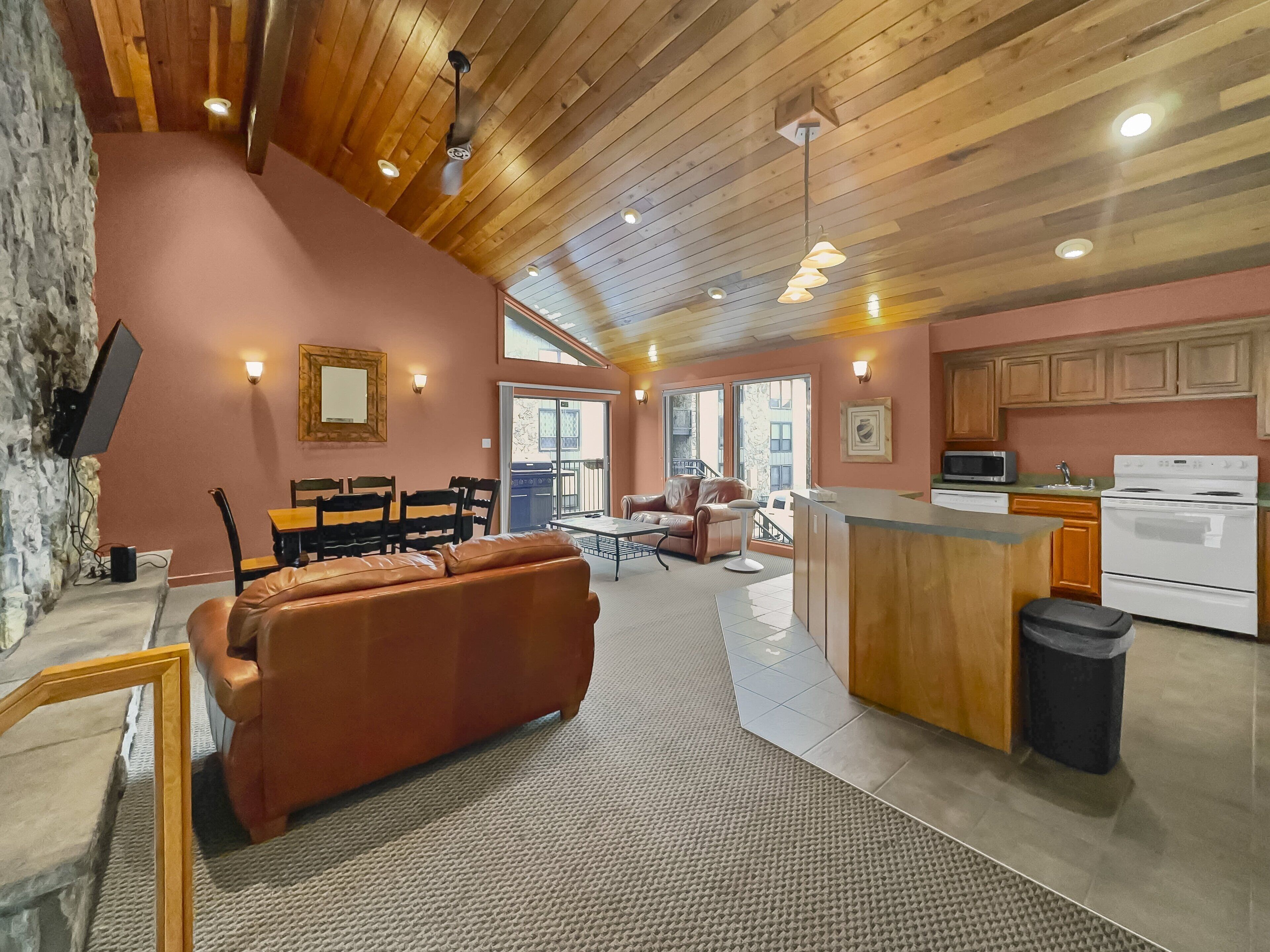 A cozy interior with a wooden ceiling, a kitchen with white appliances, and a seating area with a leather sofa and chairs.