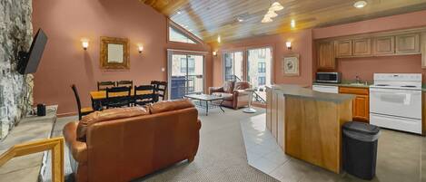 A cozy interior with a wooden ceiling, a kitchen with white appliances, and a seating area with a leather sofa and chairs.