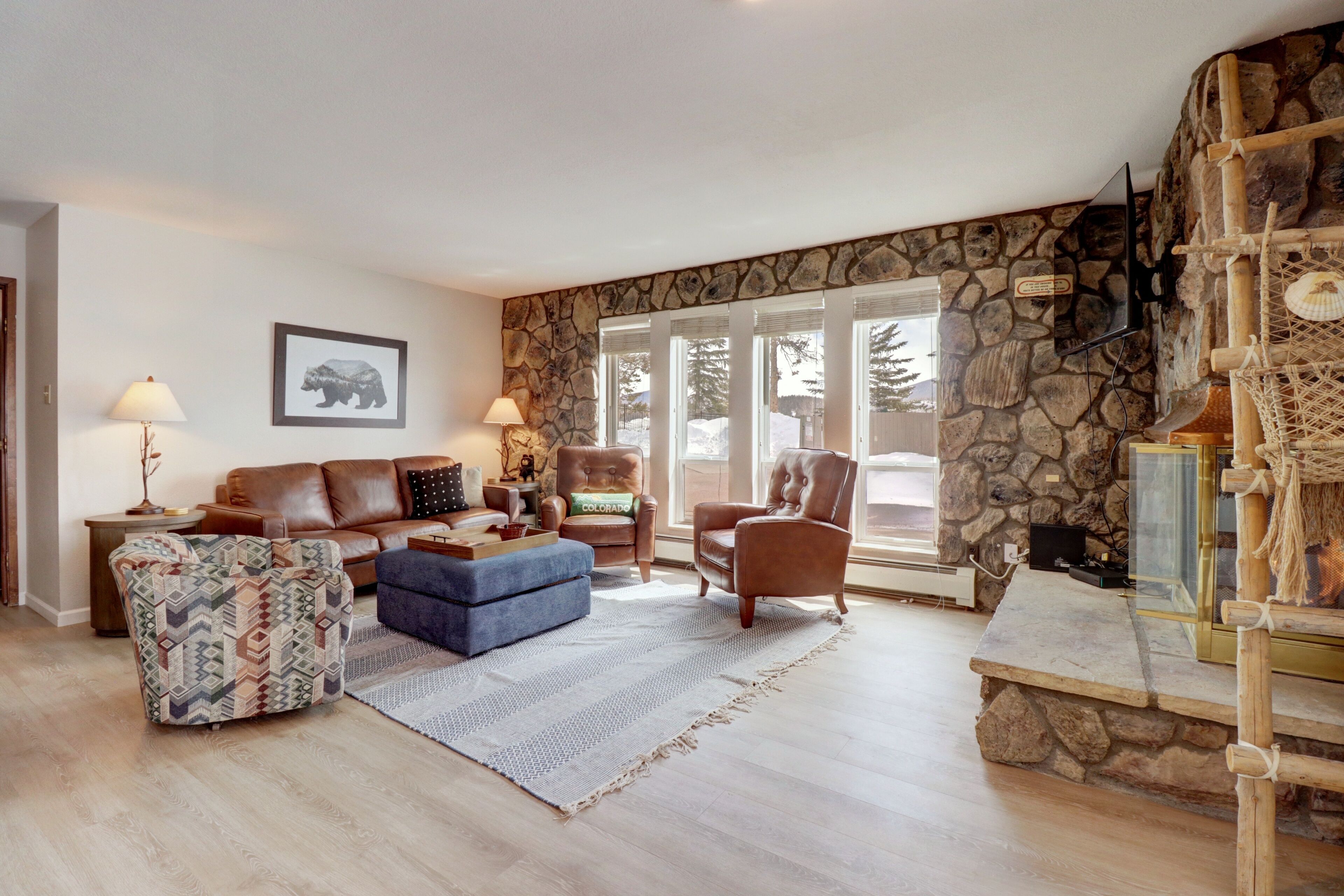 A cozy living room with a stone wall, a fireplace, and a large window.