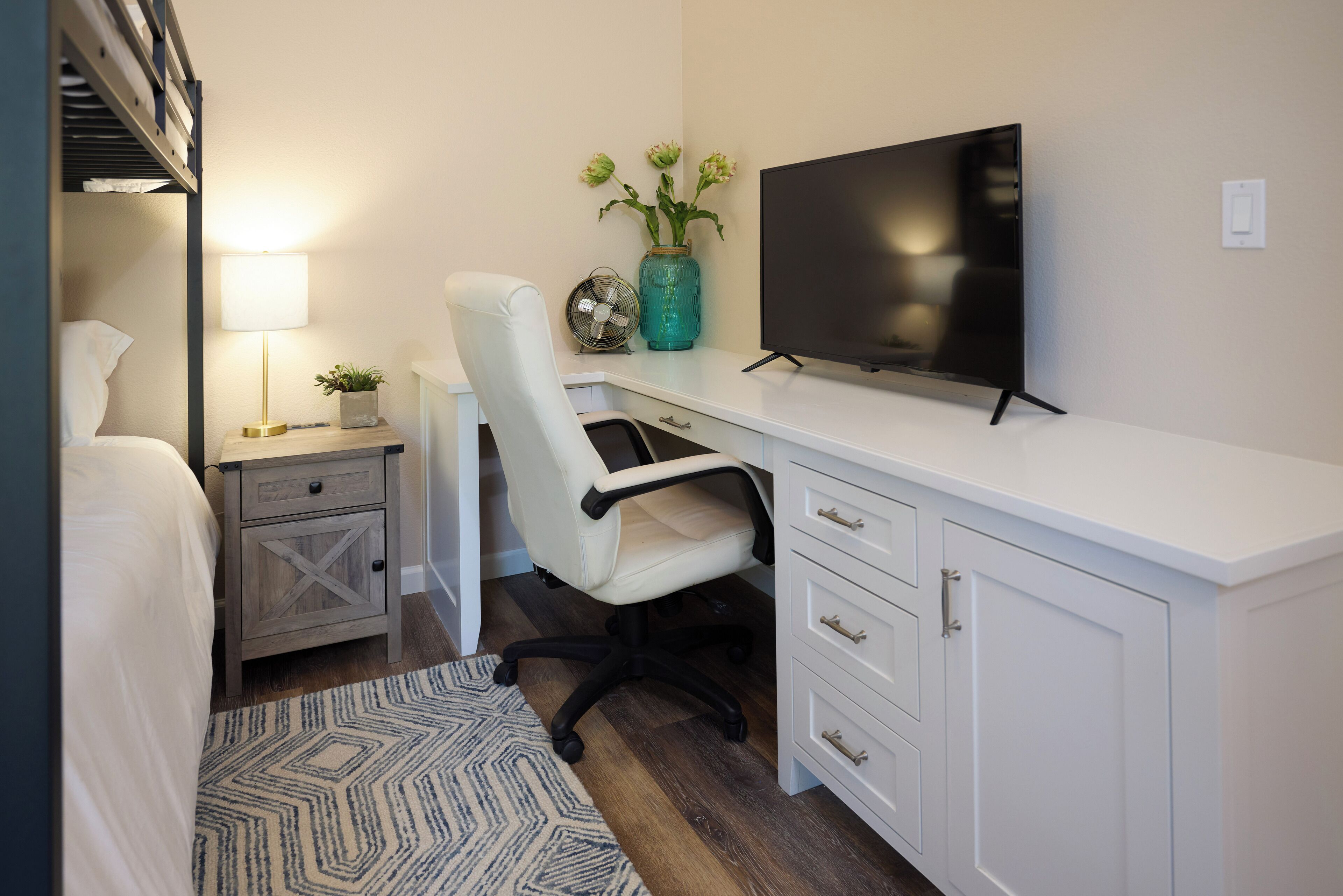 Une chambre à coucher comprenant un lit, une table de chevet, une lampe, un bureau avec une chaise et un téléviseur.