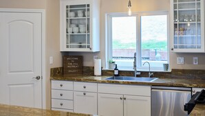 A kitchen with white cabinets, a granite countertop, a stainless steel dishwasher, and a window with a view of greenery.