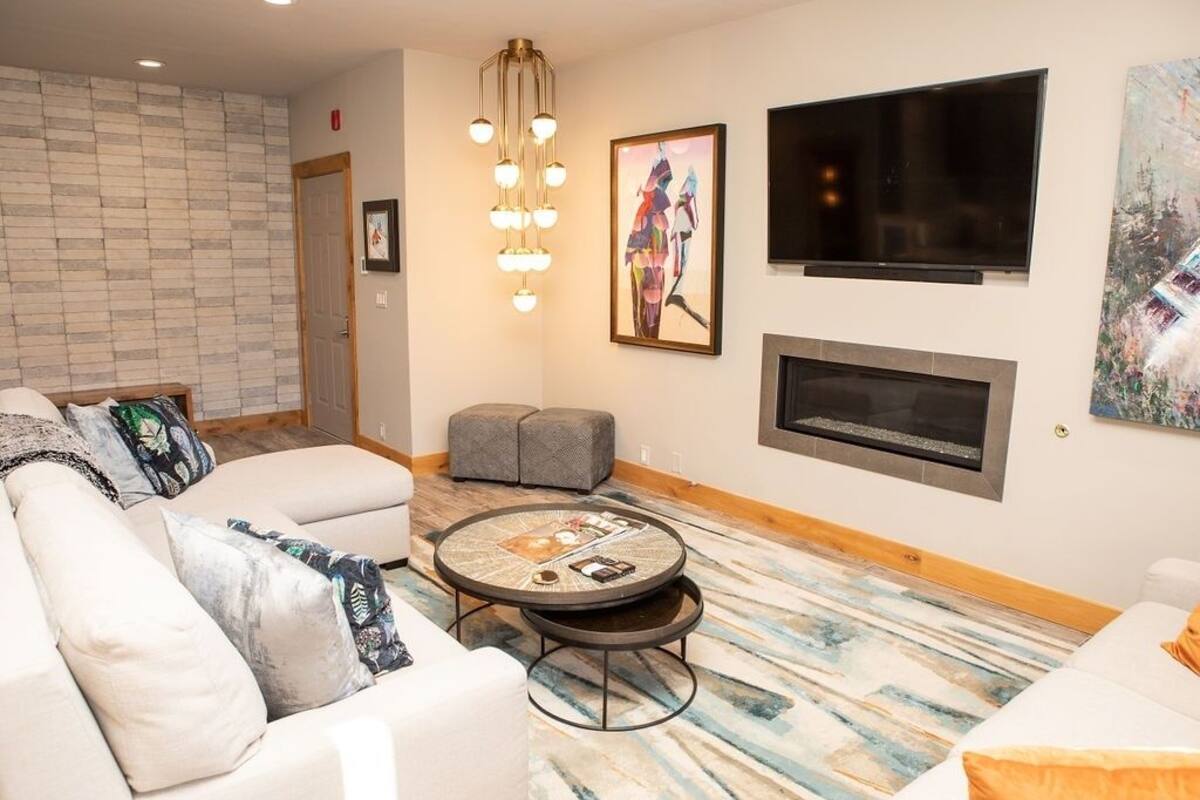 A modern living room with a sofa, ottoman, round coffee table, fireplace, TV, and artwork.