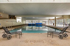 Una piscina interna con vista diretta, due poltrone relax e un muro finestrato.