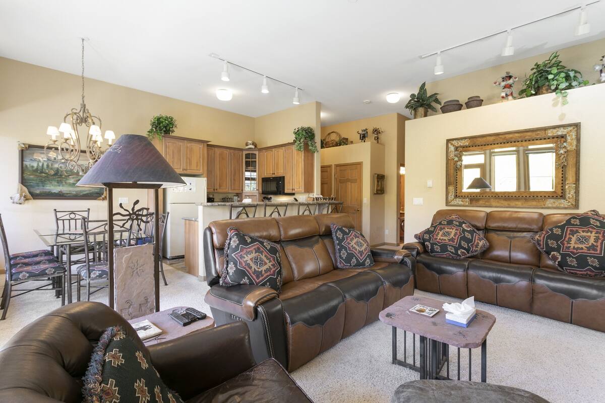 A spacious living room with leather sofas, a dining area, and a kitchen in the background.