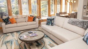 A modern living room with two sofas, a coffee table, and large windows offering a view of trees. - Vail Ski Resort Valley Condos (Vail)
