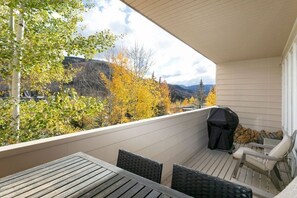 Un balcone con un tavolo e sedie di legno, un barbecue e una pila di legna da ardere.
