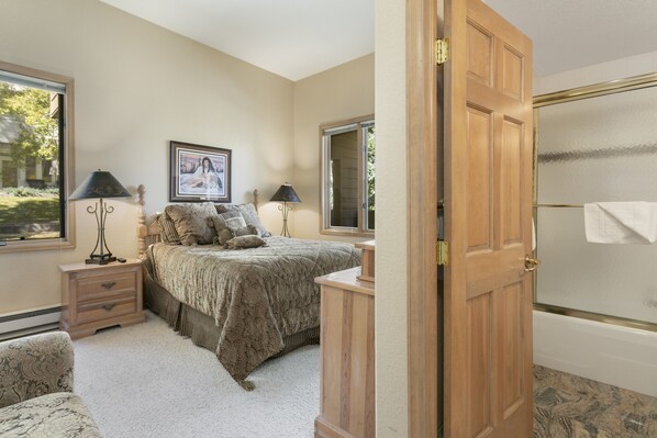 A bedroom with a bed, nightstands, a window, and a door leading to a bathroom.