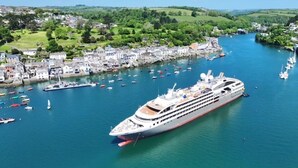 A large cruise ship docked at a harbor with a town and green hills in the background. - The Slipway Suite, Fowey Harbour & Parking 1 Min (Fowey)