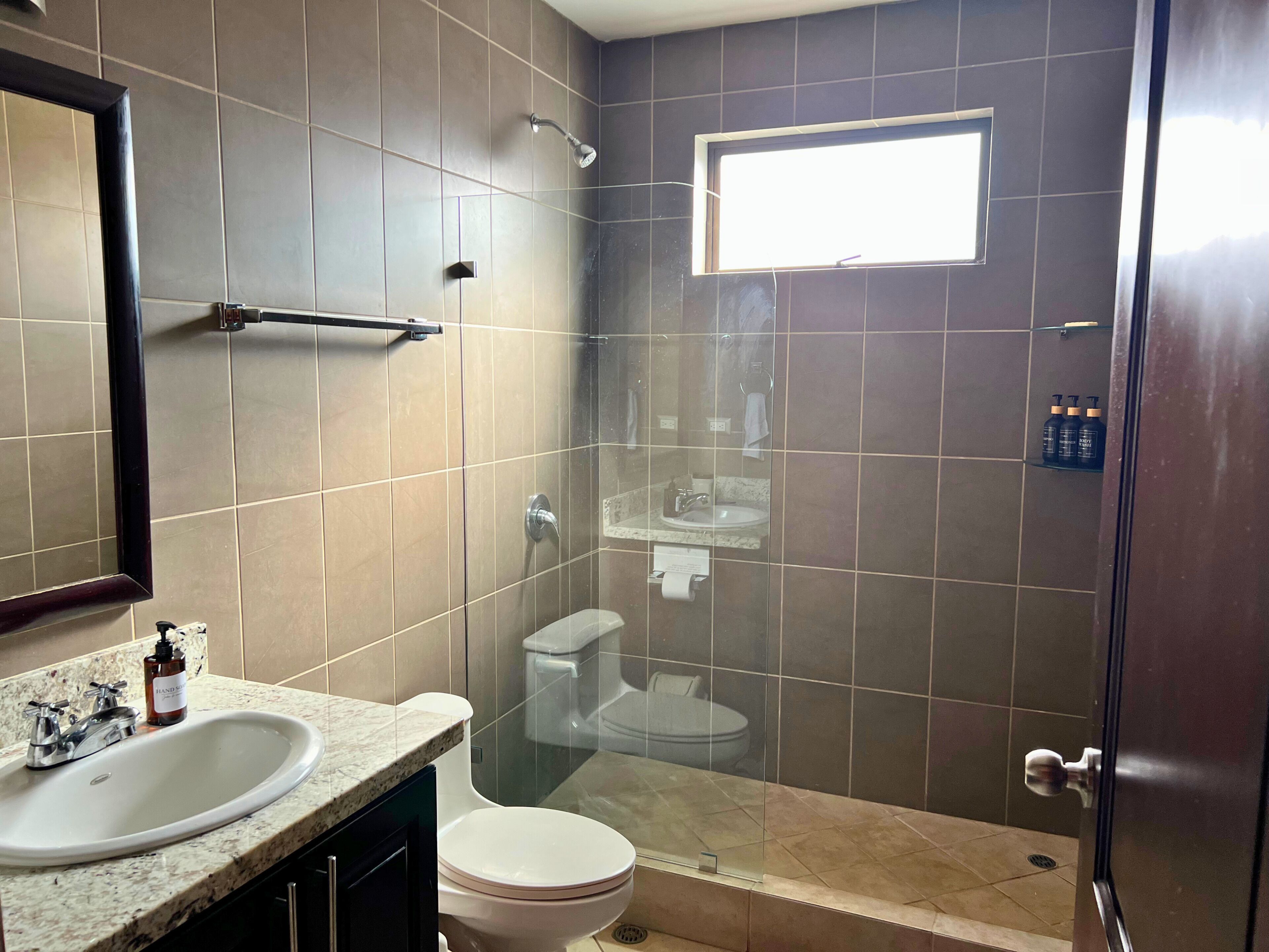 Une salle de bain moderne avec un grand miroir, un lavabo, des toilettes et un espace douche.