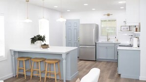 A modern kitchen with a central island, bar stools, a refrigerator, and pendant lighting.