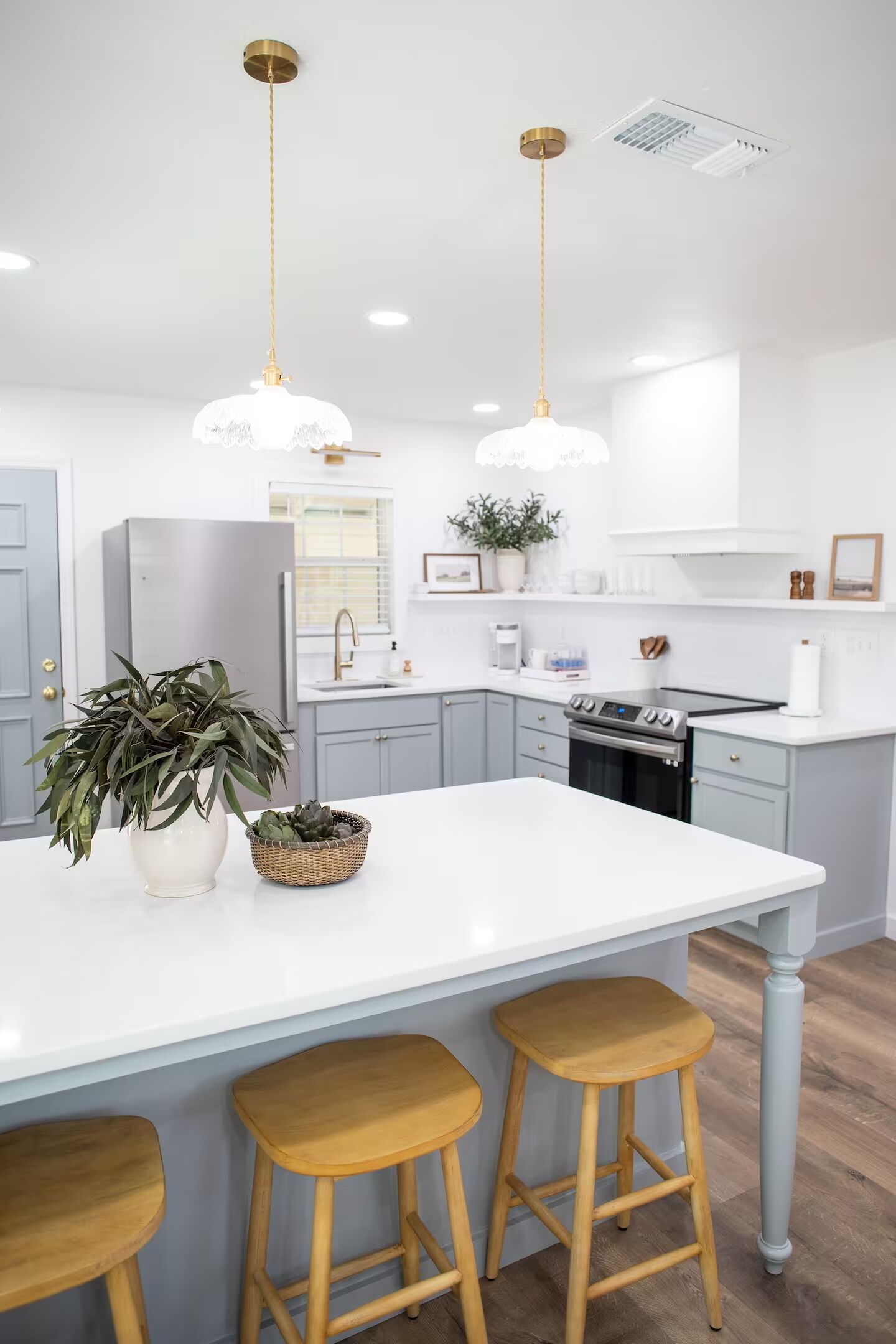 A modern kitchen with a large island, wooden stools, stainless steel appliances, and pendant lighting.