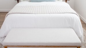 A neatly made bed with a white duvet, a matching bench, and two pillows.