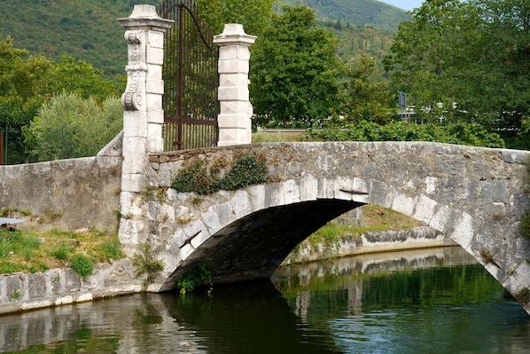 A stone bridge over a calm river, surrounded by greenery and hills.