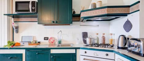 Una cucina compatta con microonde, fornelli, forno e diversi utensili da cucina.