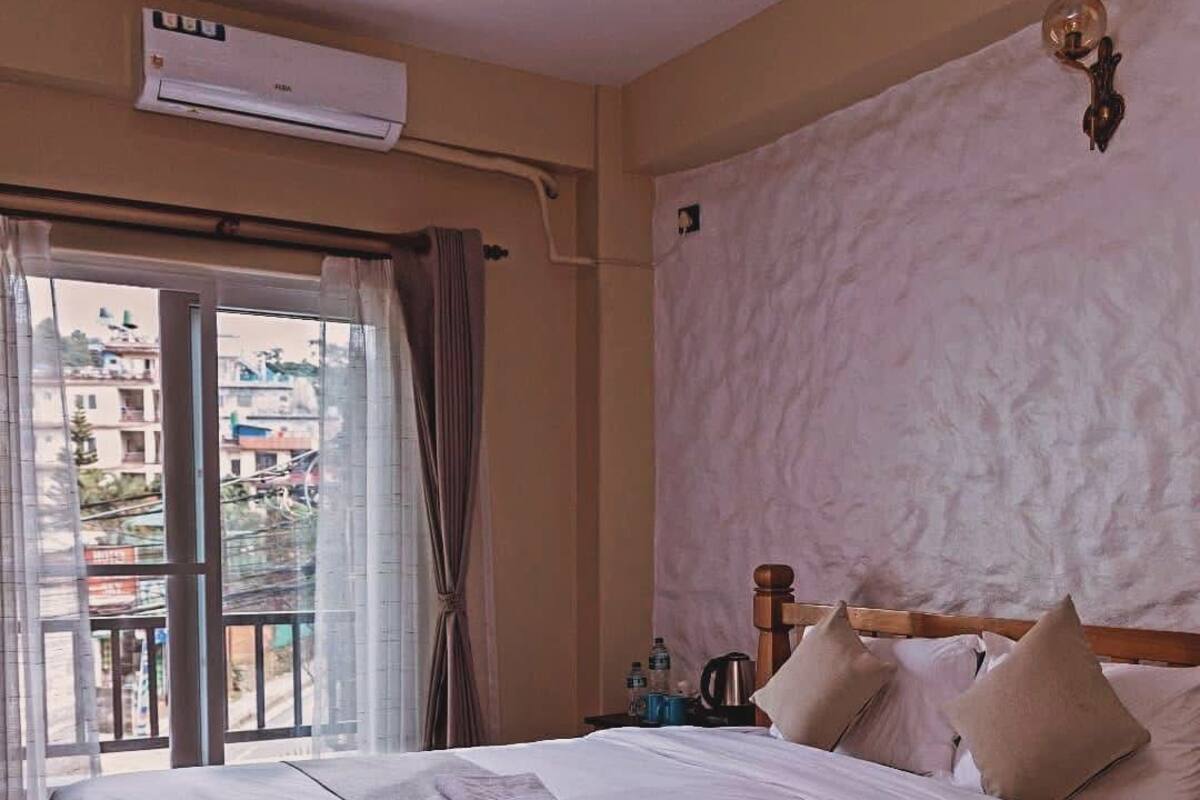 Une chambre d’hôtel avec un lit, une fenêtre avec des rideaux, un appareil de climatisation et une vue sur les bâtiments environnants.
