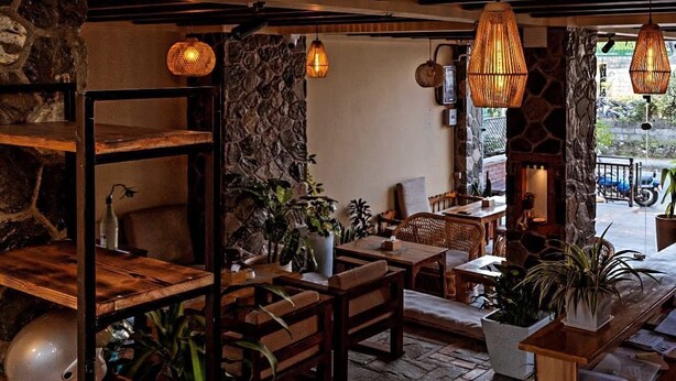 A cozy restaurant with wooden furniture, stone walls, and hanging wicker lamps. - Cozy Home (Pokhara)