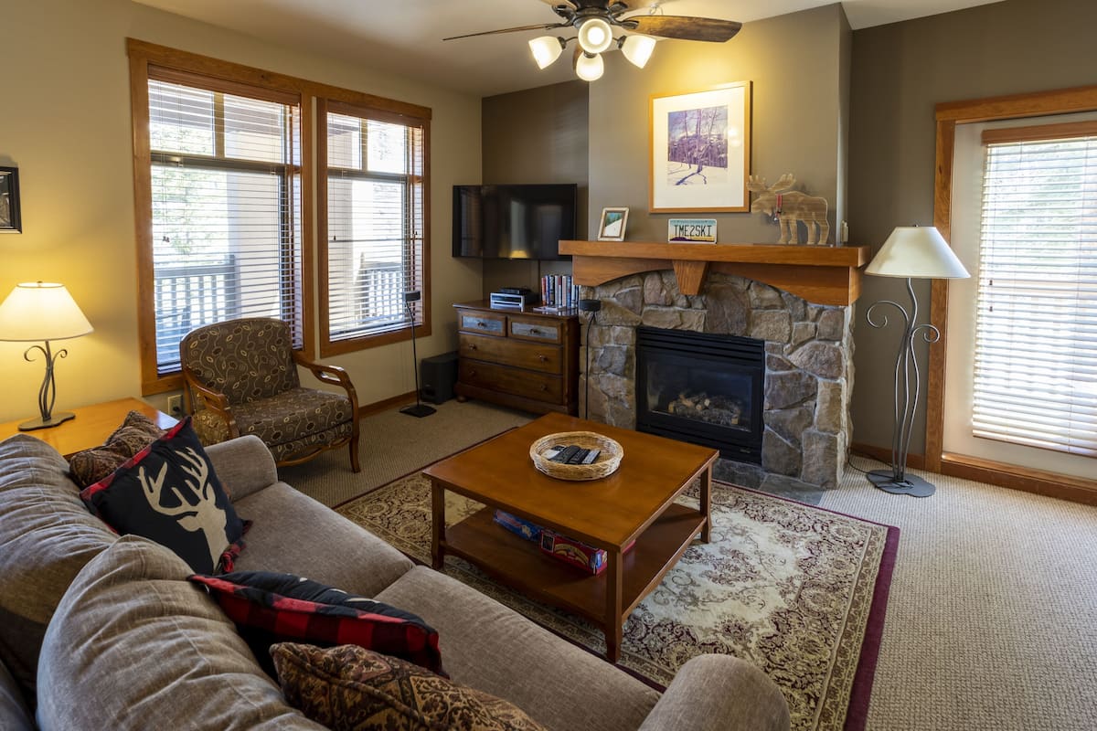 A living room with a stone fireplace, a television mounted above it, and a ceiling fan.