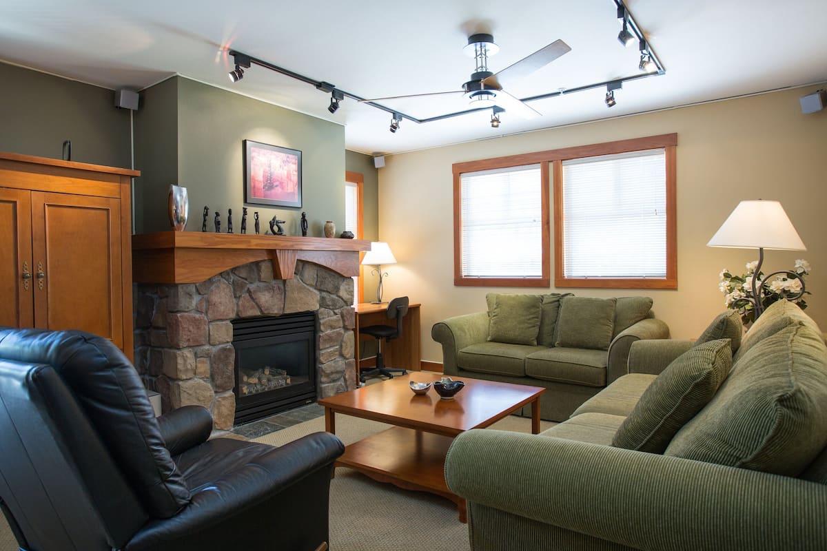 A living room with a fireplace, leather sofa, green couch, and a wooden coffee table.