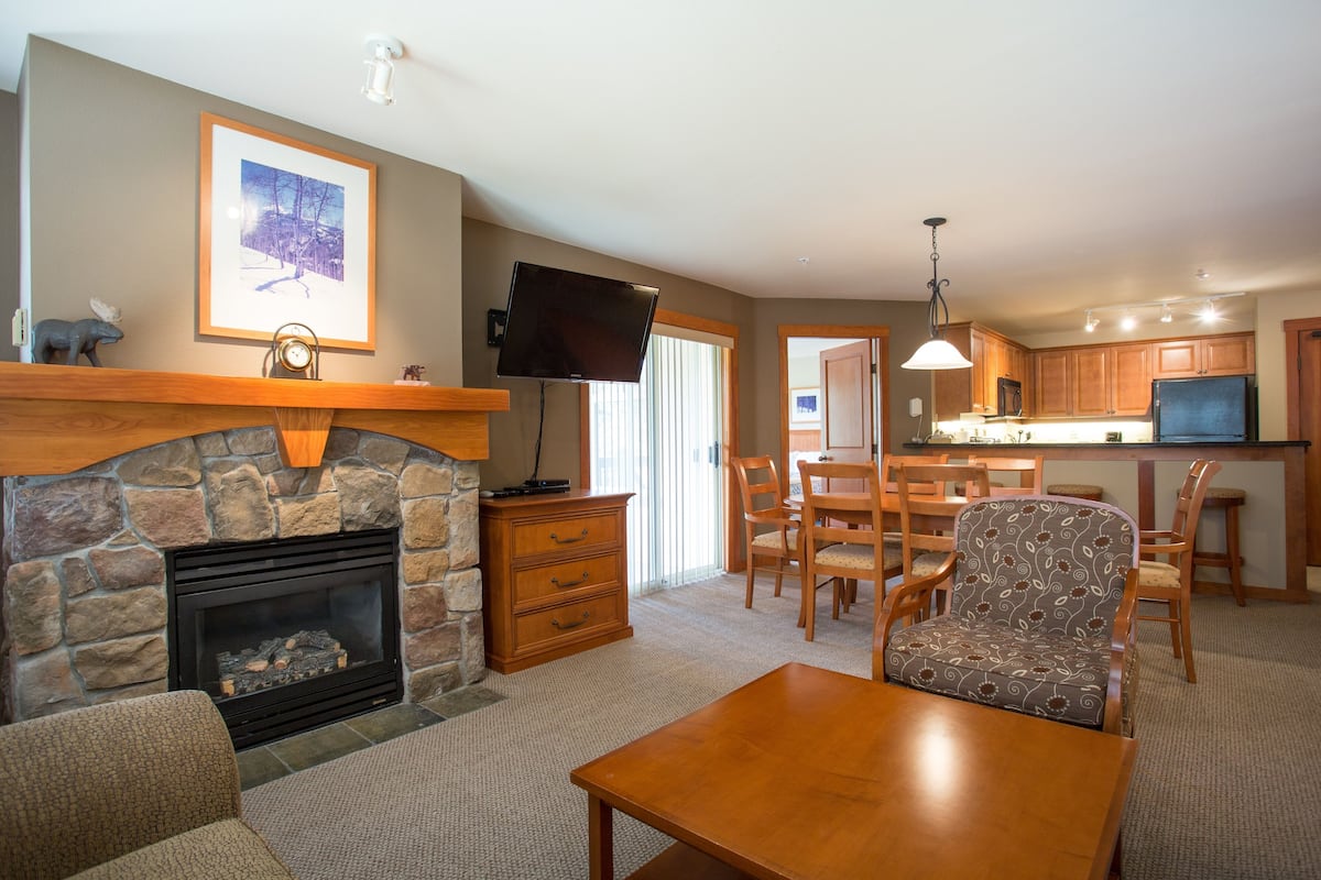 A living room with a stone fireplace, wooden furniture, and a television mounted on the wall.