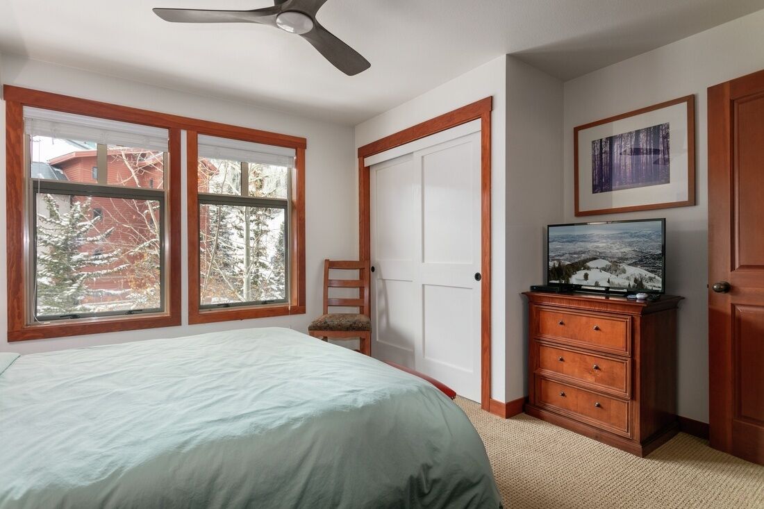 Ein Schlafzimmer mit einem Bett, einer Kommode, einem Fernseher und einem Deckenventilator.