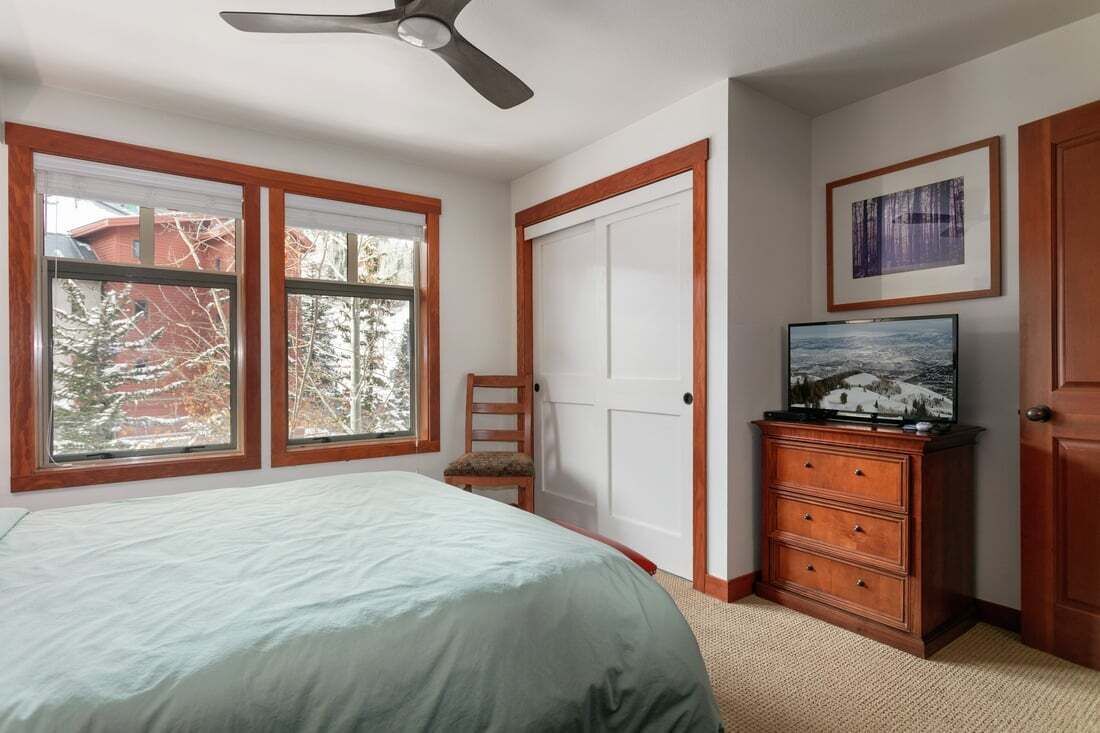 A bedroom with a bed, a dresser, a television, and a window with a view of trees.
