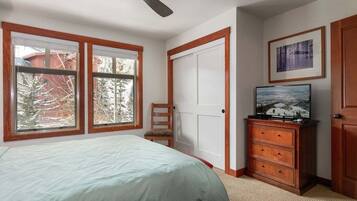 A bedroom with a bed, a dresser, a television, and a window with a view of trees.