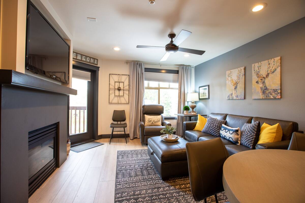 A modern living room with a fireplace, leather sofa, and a ceiling fan.