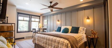 A bedroom with a large bed, a ceiling fan, a nightstand, and a window with a view of trees.